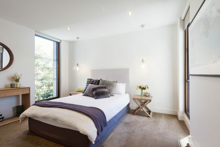 A double-size bed with pillows, two side tables with pendant lights hanging from the ceiling, huge glass windows