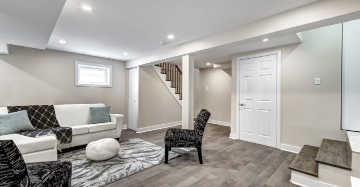 A basement with a white sofa set and floor rug, and cushioned printed black chairs