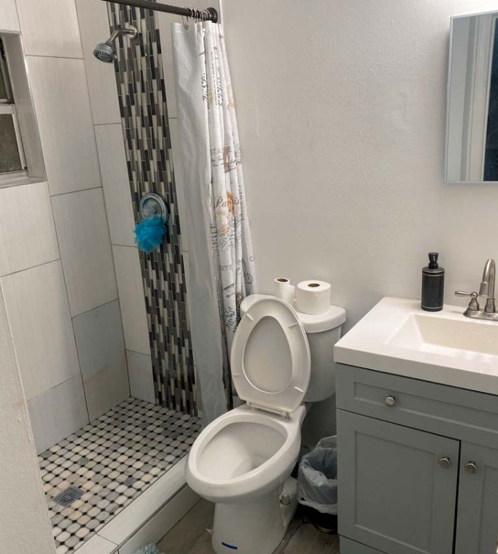 A bathroom toilet, a shower area, separated by curtains. a sink cabinet. and a mirror