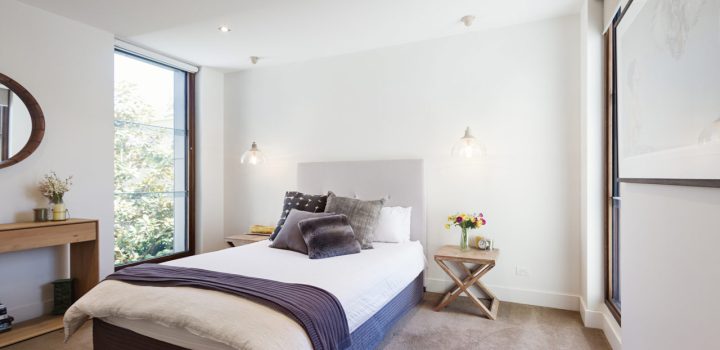 A double-size bed with pillows, two side tables with pendant lights hanging from the ceiling, huge glass windows