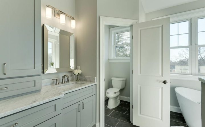 A bathroom wherein there is a door to separate the toilet in one corner, a free standing modern tub, and a vanity area