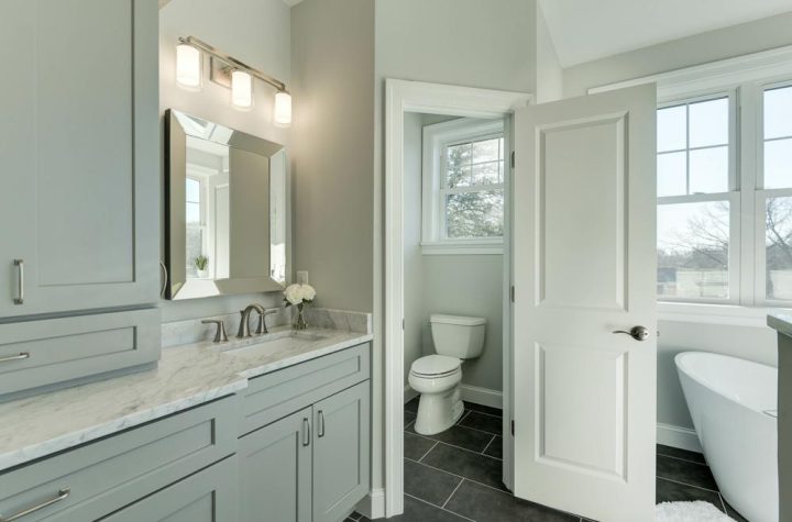 A bathroom wherein there is a door to separate the toilet in one corner, a free standing modern tub, and a vanity area