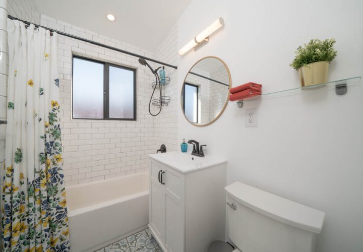 Modern interior bathroom shower sink toilet design, a circular mirror, a floral shower curtain, a lavatory and a plant on the toilet shelf