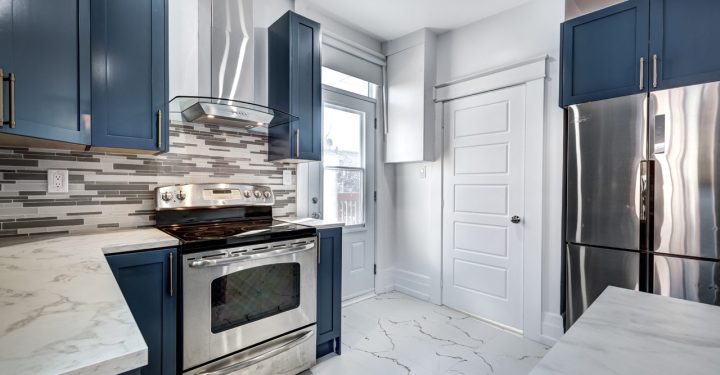 A kitchen following a blue color scheme, ceramic tiles, a granite countertop, a stove with hood, oven, and a refrigerator