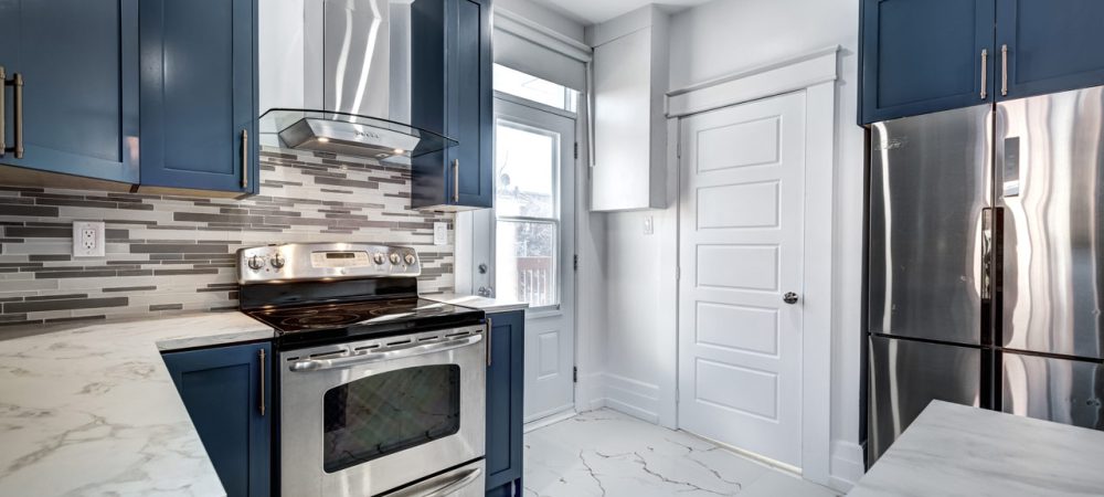 A kitchen following a blue color scheme, ceramic tiles, a granite countertop, a stove with hood, oven, and a refrigerator