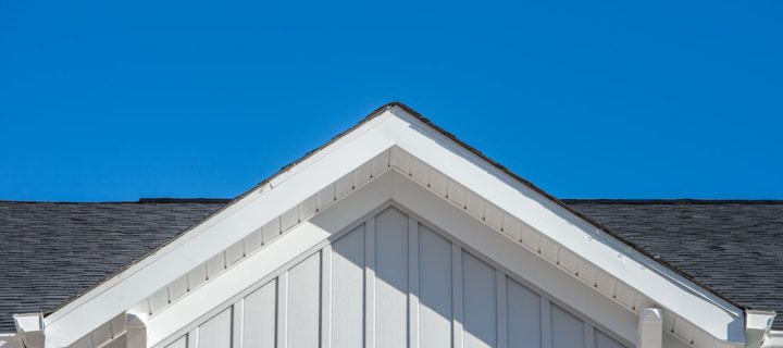 Gable roof with white fascia, gray vertical vinyl lap siding on a blue sky background