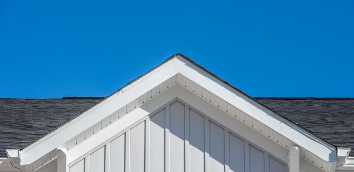 Gable roof with white fascia, gray vertical vinyl lap siding on a blue sky background