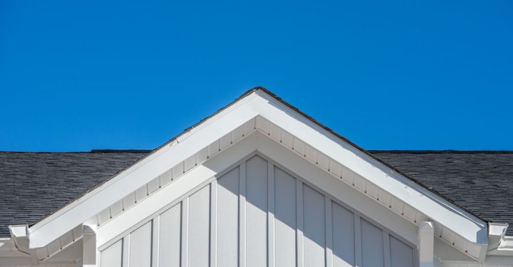 Gable roof with white fascia, gray vertical vinyl lap siding on a blue sky background