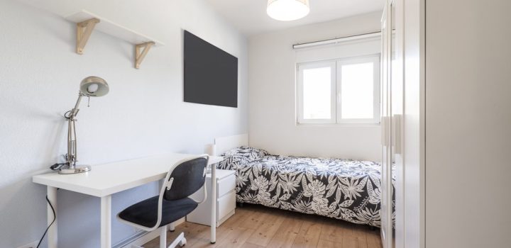 A modern bedroom with study or work desk and chair, a wall mounted flat screen, a cabinet, and a side table with drawers